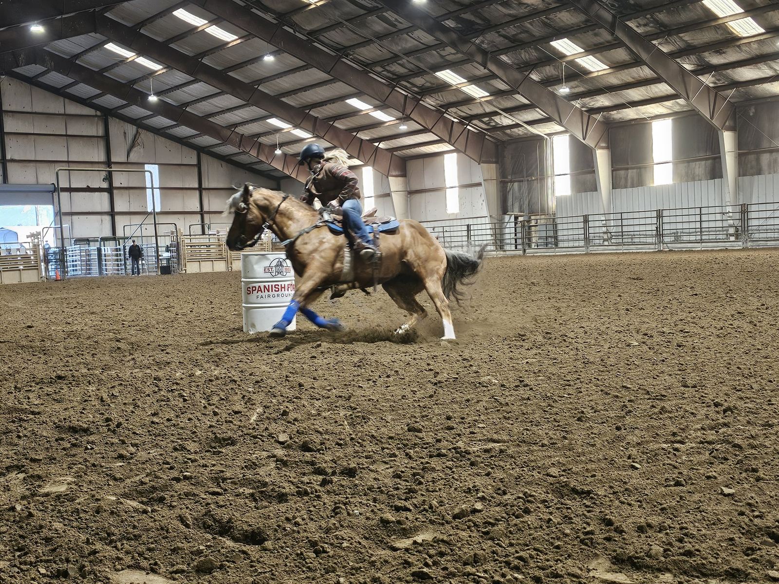 A rider on a palomino horse turning tight around a barrel, dirt flying