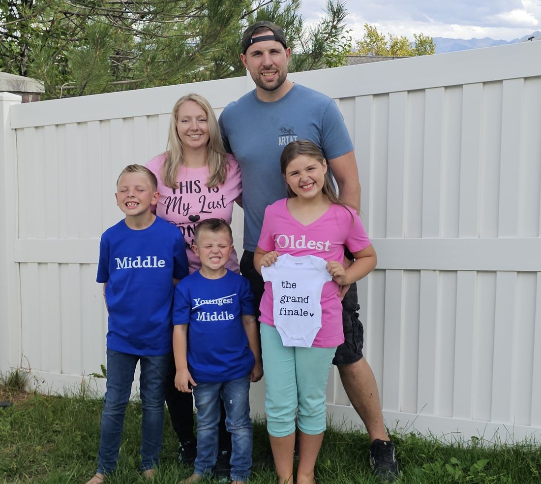 Matthew and Alena with their three kids in Oldest, Middle and Middle shirts, holding a baby onesie that reads the grand finale