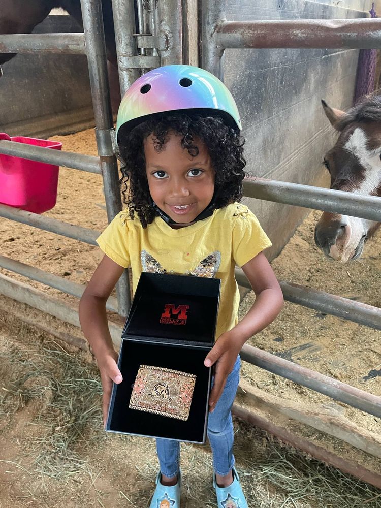 A young girl in a rainbow helmet holding her Lead Line Champion buckle